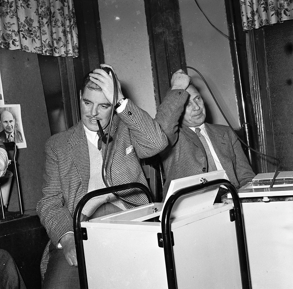 Two men in a 1950s studio, hands on their heads