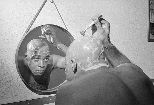 A man shaving his head in a round mirror